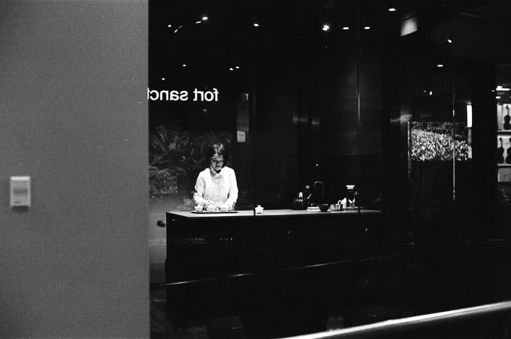 Photo of a lady mending to fine china under a spotlight in a darkened room, behind a glass store front.